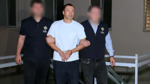 Georgian State Security Service A man in a white T-shirt is held by the arms by two men in dark-coloured uniform